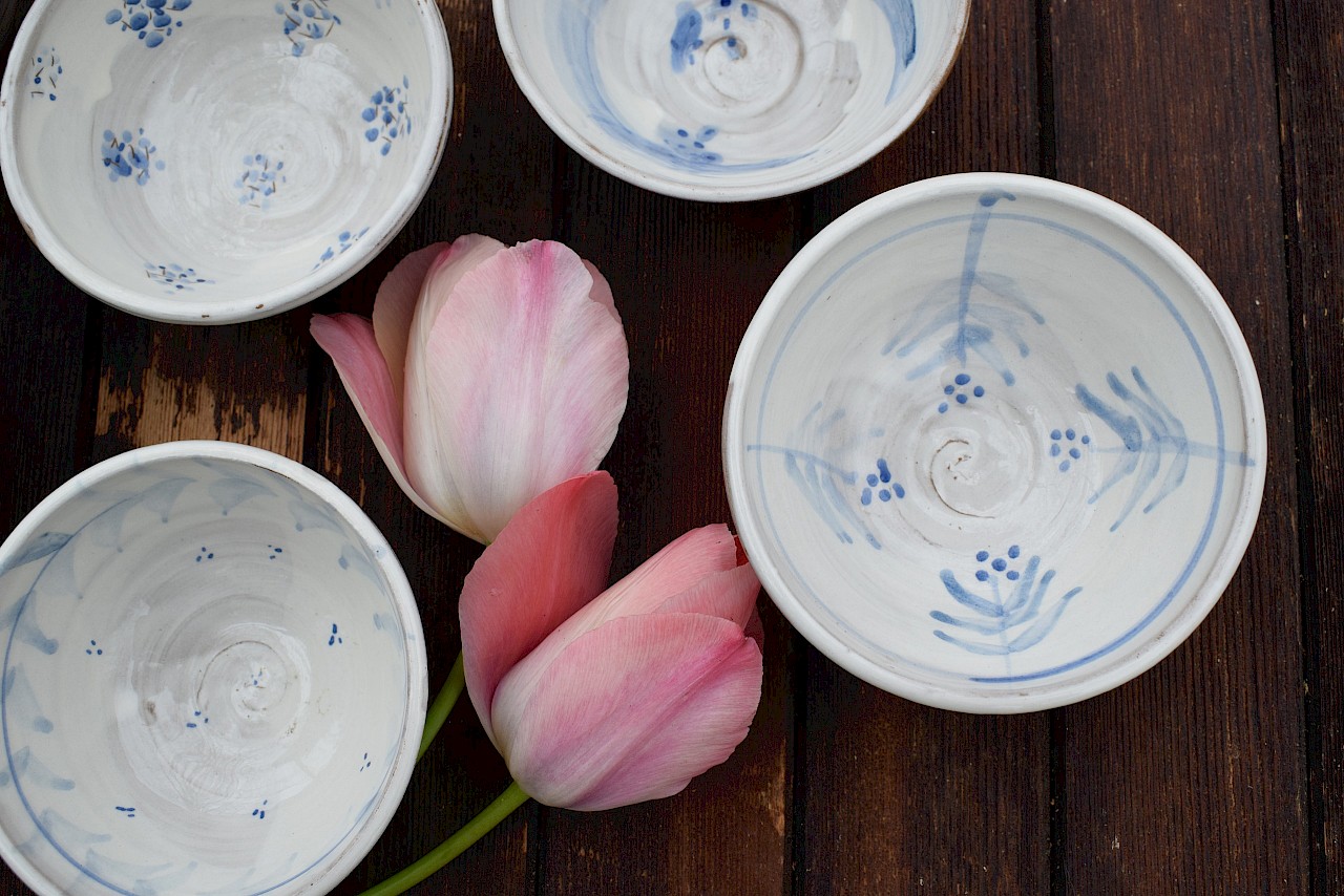Weiße Keramikschalen mit blauer Bemalung und zwei rosa Tulpen auf einem Holztisch